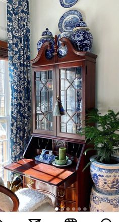 a blue and white china cabinet sitting next to a potted plant in front of a window