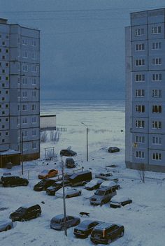 cars are parked in the snow near tall buildings