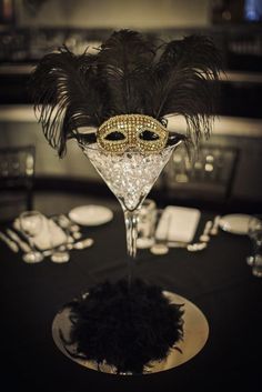 a masquerade mask sitting on top of a glass filled with wine glasses and silverware