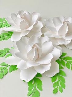 paper flowers are arranged on a white surface with green leaves and branches in the center