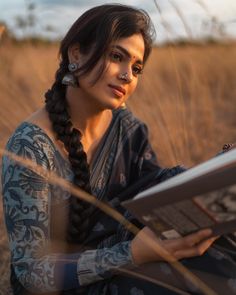 a woman with braids reading a book in a field at sunset or sunrise time