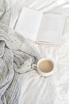 a cup of coffee and an open book on top of a bed with white sheets