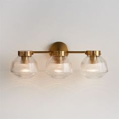 three glass globe lights mounted on the wall above a vanity light in an antique brass finish