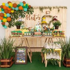 a table topped with lots of food and plants next to a wall covered in balloons