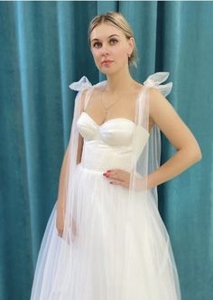 a woman in a white wedding dress standing next to a blue curtain with her hands on her hips