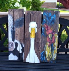 three painted wooden boards sitting on top of a bench next to a cow and chicken