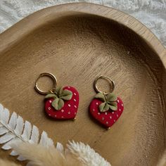 two red strawberry shaped earrings sitting on top of a wooden tray