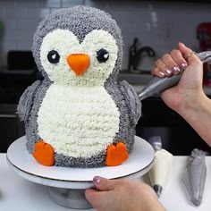 a cake shaped like a penguin being frosted by someone's hand with a knife