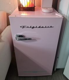 a pink refrigerator sitting next to a white couch in a living room with a lamp on top of it