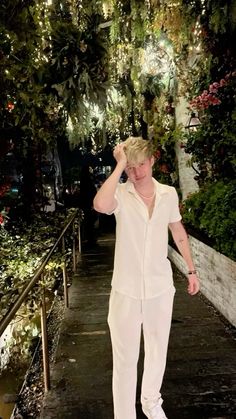 a young man walking down a sidewalk next to a lush green tree filled forest at night