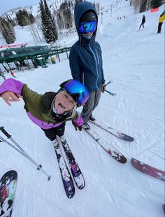 two children on skis in the snow with their arms out and one child wearing goggles