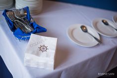 a table topped with plates and silverware next to a blue cloth covered napkin on top of a white tablecloth