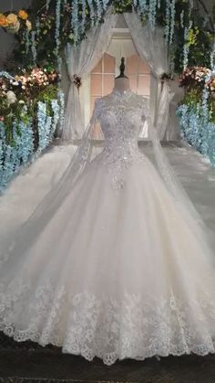 a white wedding dress on display in front of a floral arch with blue flowers and greenery