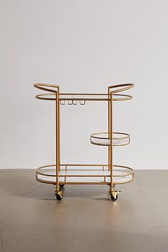 a gold serving cart with three trays on wheels and one holding two drinks glasses