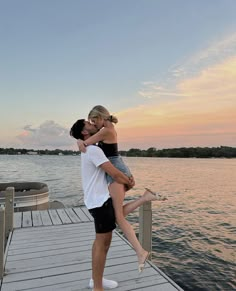 a man holding a woman on top of a wooden dock near the water at sunset