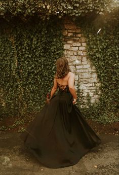 the back of a woman's black dress in front of a brick wall with ivy growing on it