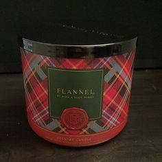 a red and black plaid candle on a wooden table next to a bottle of flannel