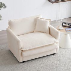 a white chair sitting on top of a rug next to a coffee table and lamp