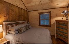 a bed in a bedroom next to a lamp and window with wood paneling on the walls