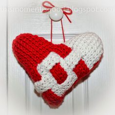 a crocheted heart hanging on a door with a red and white decoration attached to it