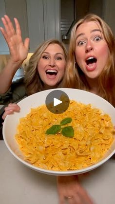 two women holding up a large plate of noodles