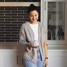 a woman standing next to a kitchen counter holding a ball of yarn in her hands