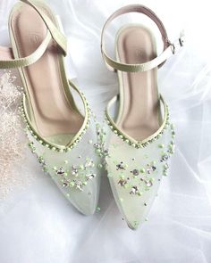 a pair of white high heel shoes with green beading on the toes and straps