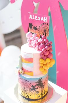 a multi - tiered cake decorated with colorful candies and palm trees sits on a table