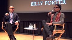 two men sitting in chairs talking to each other at a public event with a screen behind them