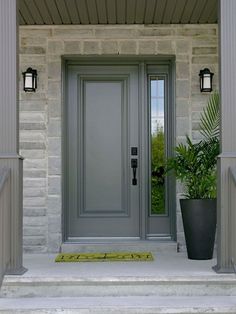 a gray front door with the letter m on it's side and potted plant next to it