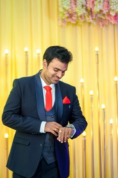 a man in a suit and red tie is looking down at his watch while standing next to a yellow curtain