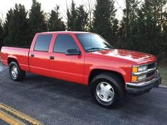 a red pick up truck parked in a parking lot next to some bushes and trees