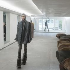 a woman is standing in an empty room with her coat over her shoulders and boots on