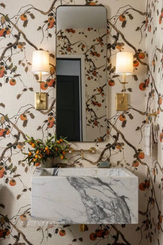 a marble sink in front of a mirror and wallpaper with oranges on it