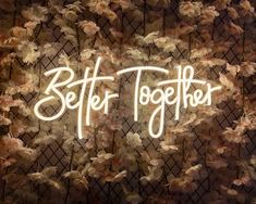 a neon sign that says better together in front of some pink and white flowers on a wall