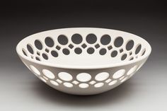 a white bowl with holes in it on a gray surface, sitting on a table