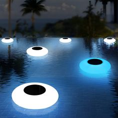 an outdoor swimming pool with blue and white lights on the water, surrounded by palm trees