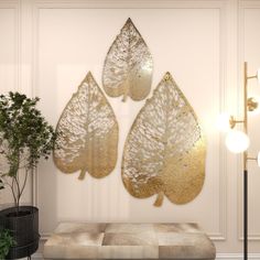 three gold leaf shaped wall hangings on a white wall next to a potted plant