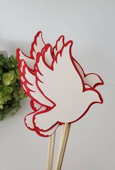 a red and white paper bird on top of some toothpicks with flowers in the background