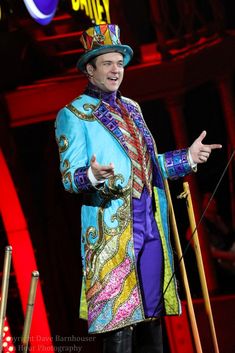 a man in a colorful suit and top hat on stage with his hands out to the side