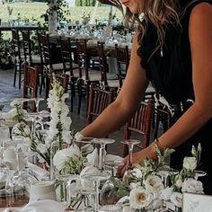 a woman standing over a table filled with lots of white flowers