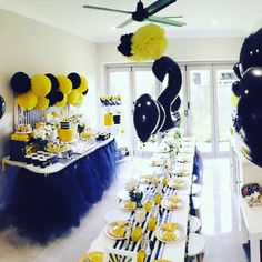 a black and yellow party with balloons, streamers, plates and desserts on the table