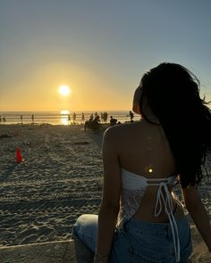 a woman is sitting on the beach watching the sun go down and people are in the background