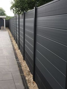 a long black fence is next to a sidewalk and trees on the other side of the fence