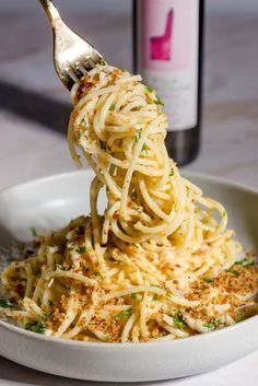 a fork full of spaghetti being lifted from a white bowl with parmesan cheese