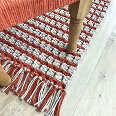 an orange and white rug on the floor next to a wooden chair with a brown foot rest