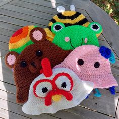 four crocheted hats are sitting on a wooden table with the faces of different animals