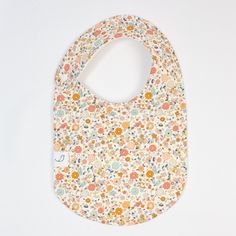 a bib with flowers on it sitting on a white surface, the bib has a small hole in the middle