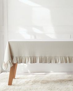 a white table with a long ruffled cloth on it's edge and wooden legs