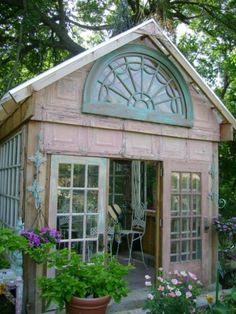 a small wooden building with lots of windows and plants in the front yard, along with potted flowers